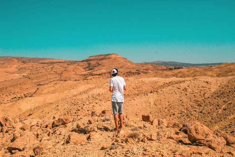 Rear view of man standing at desert against clear blue sky