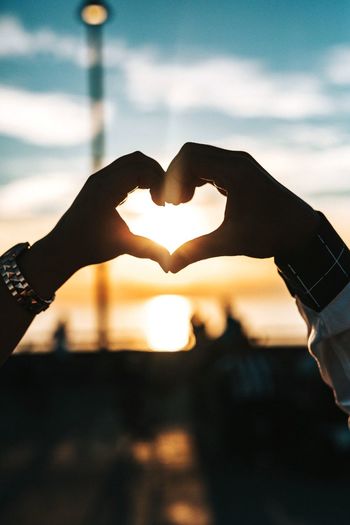 Midsection of woman making heart shape against sky during sunset