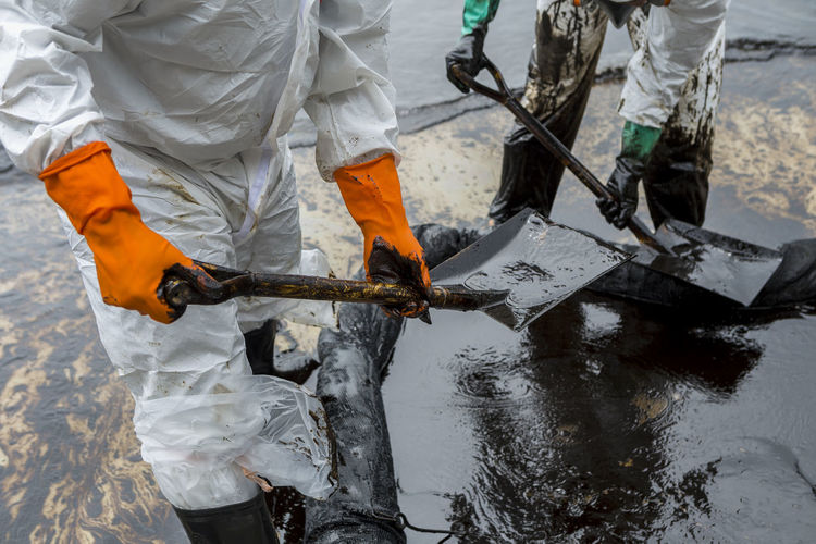 Midsection of manual worker cleaning crude oil at beach