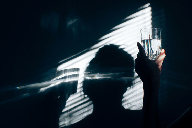 Close-up of woman with drinking glass against wall during sunny day