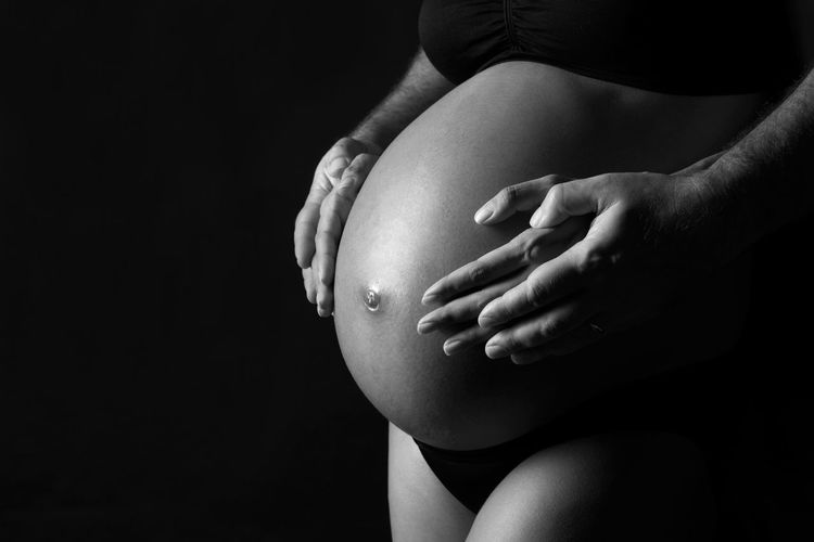 Midsection of pregnant woman touching her belly against black background