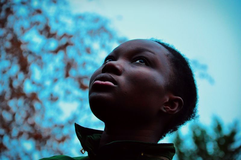 Close-up of serious young woman against blue sky