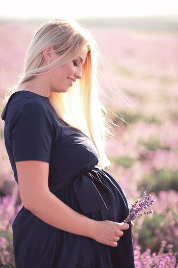 Pregnant woman with flower standing on field