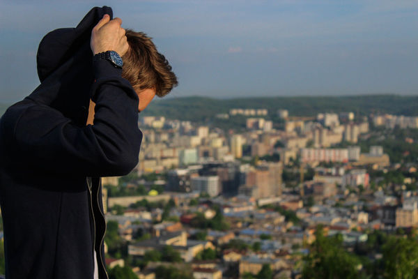 Side view of man wearing black hooded jacket against cityscape