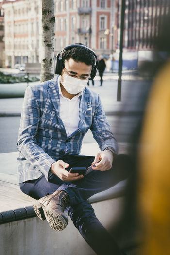 Businessman with smartphone sitting outside with face mask