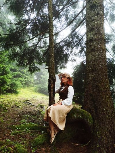 Woman by tree trunk in forest