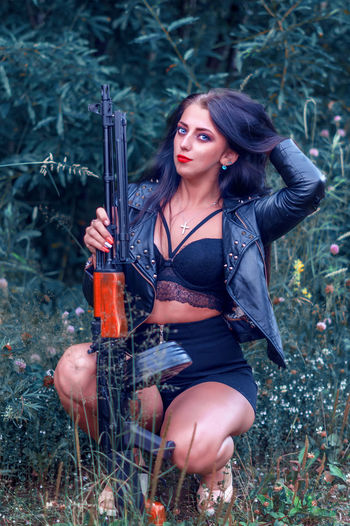 Portrait of sensuous hunter holding rifle while crouching on field