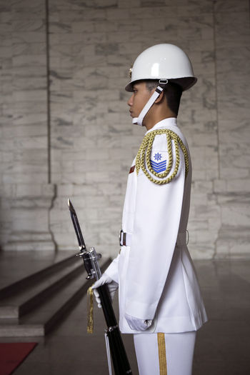 Side view of male police officer standing with gun against wall