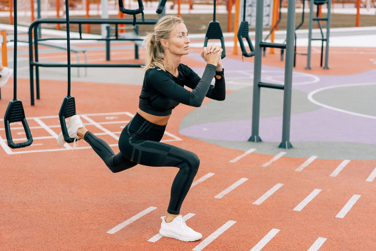 Middle-aged woman squats pumping muscle mass on the sports ground.