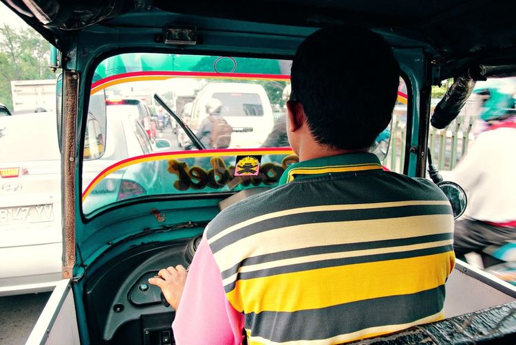 Rear view of man driving tuk tuk on road in city