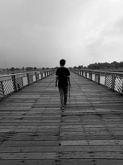 Rear view of man walking on pier against sky
