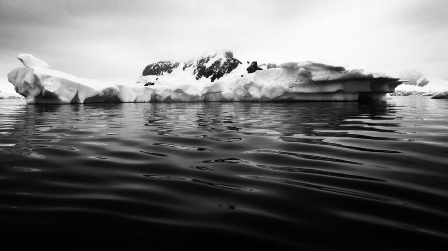 Black and white photo of iceberg with mountain in the background in antarctica