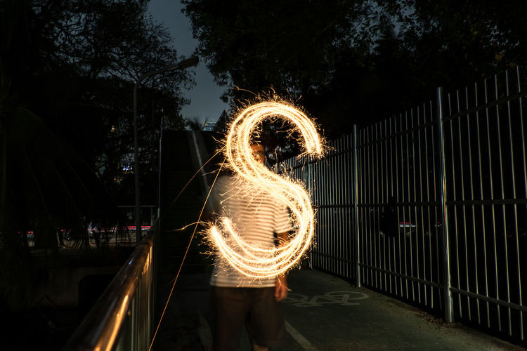 Woman standing by illuminated ferris wheel at night