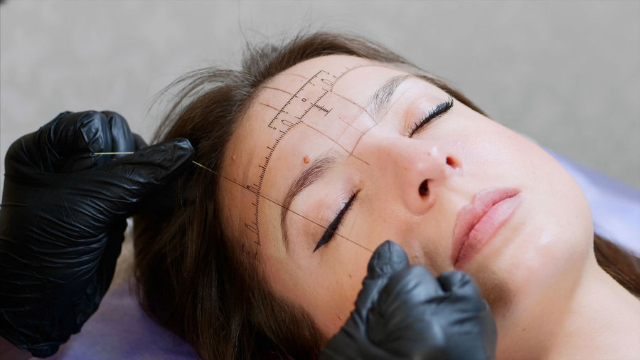 Cropped hands of beautician threading woman eyebrow