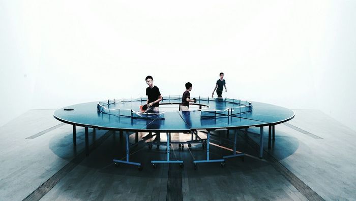 Boys playing ping pong go-round against white background