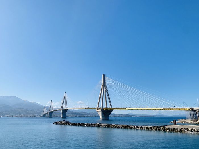 Suspension bridge over sea against clear blue sky