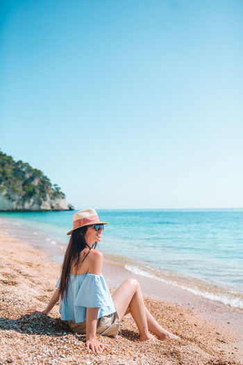 Woman sitting on beach against clear sky