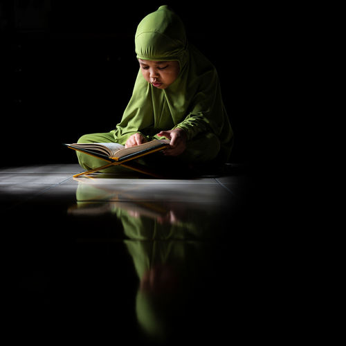Rear view of boy sitting on book against black background