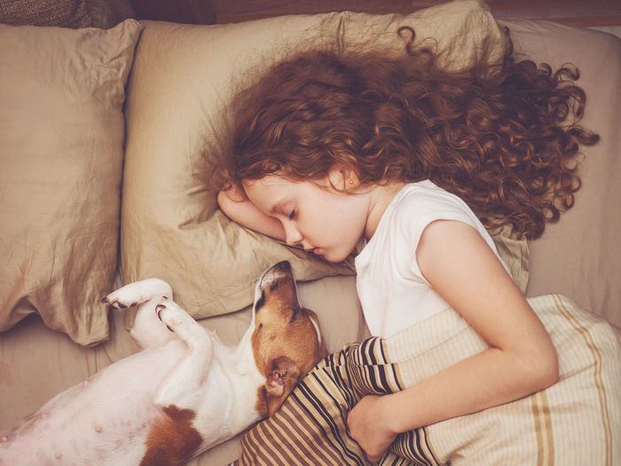 Sweet curly girl and jack russell dog is sleeping in night.