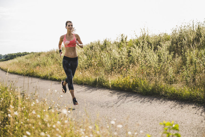 Sportswoman running on road by meadow