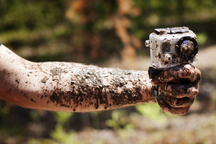 Cropped image of muddy hand holding camera
