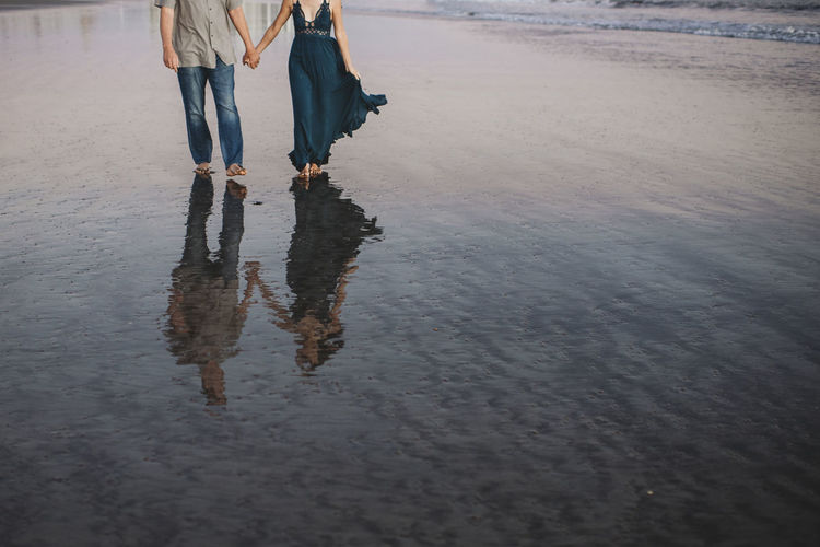 Wet sand reflection of barefoot couple walking the beach hand in hand