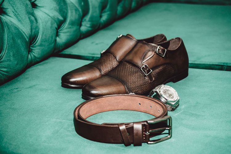 High angle view of shoes with belt and wristwatch on sofa