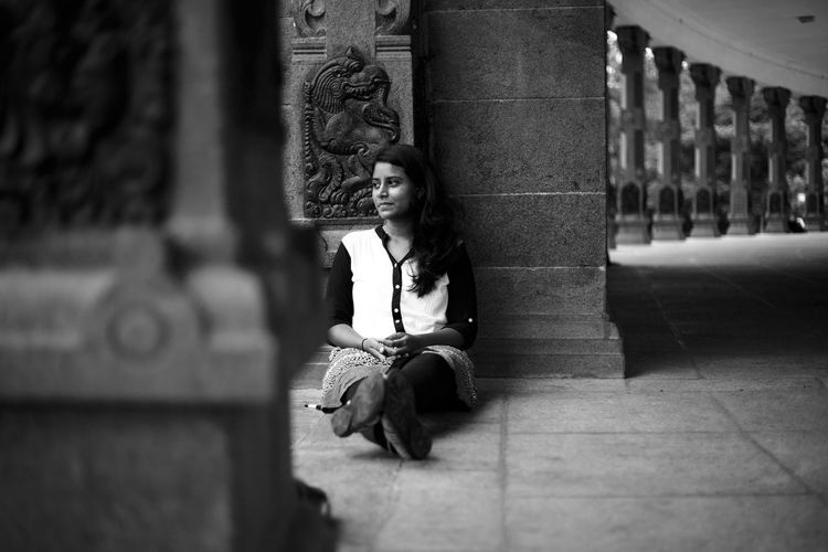 Thoughtful woman looking away while sitting against column