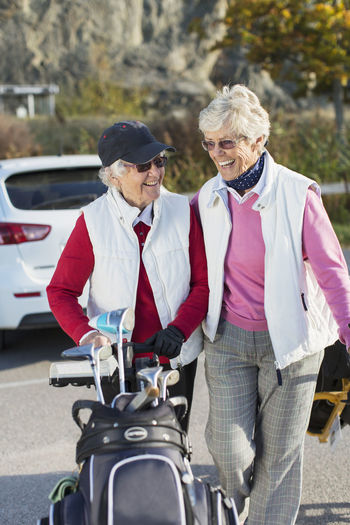Smiling senior women walking with golf bag outdoors