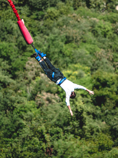 Full length of man enjoying bungee jumping over forest