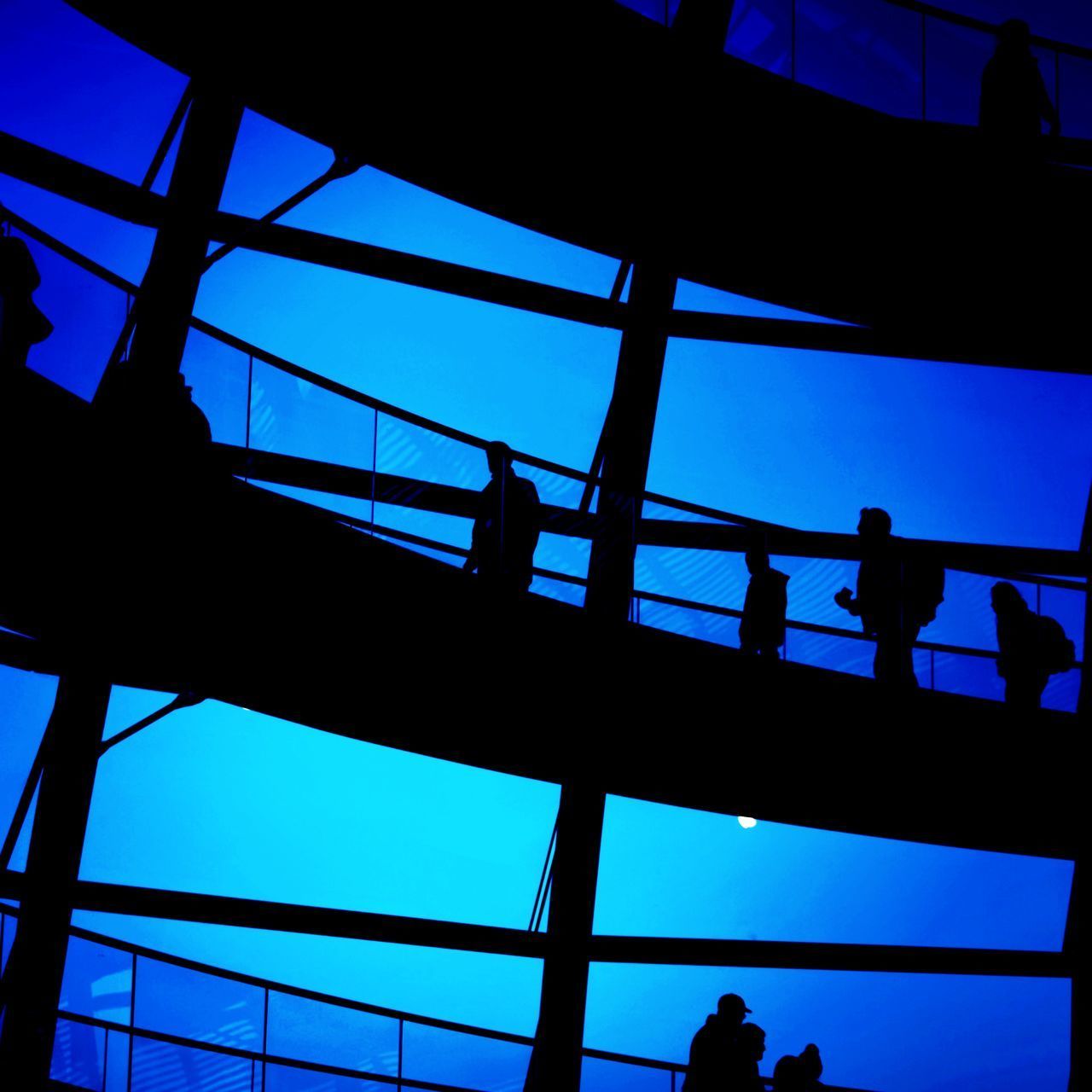 LOW ANGLE VIEW OF SILHOUETTE PEOPLE STANDING IN CITY AGAINST BLUE SKY