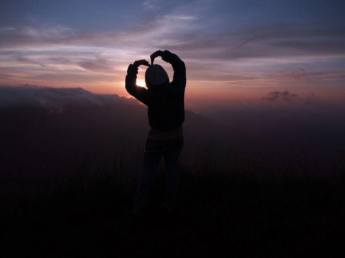 Silhouette woman making heart shape on mountain during sunset