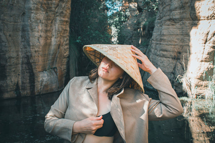 Young woman looking at camera, in nature wearing asian straw hat. 
