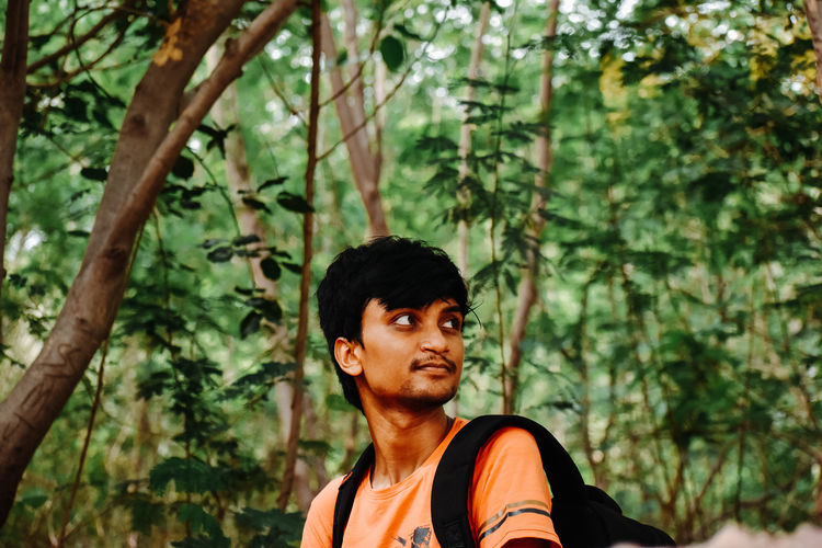 Young man looking away against trees in forest