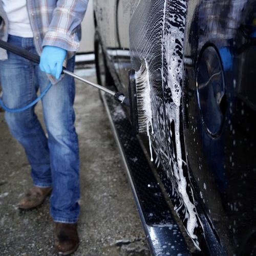 Midsection of man cleaning car with equipment in garage