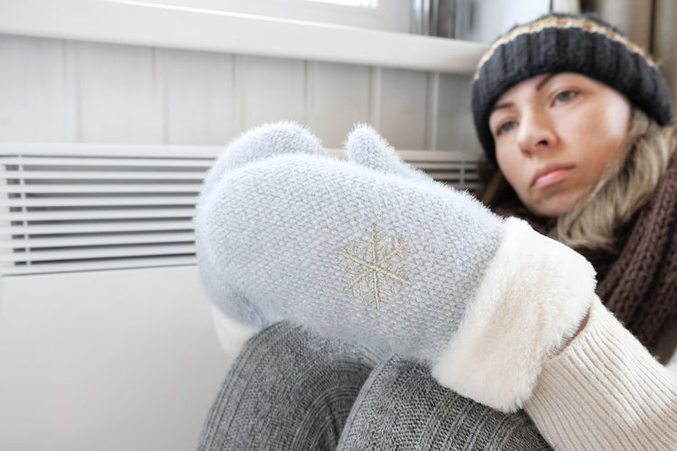 Young frozen woman wearing a sweater freezing for winter cold at home. girl is near electric heater.