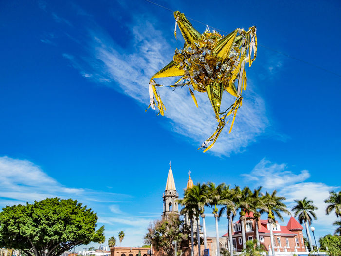 Low angle view of gold and silver pinata against blue sky, mexican cultural traditions