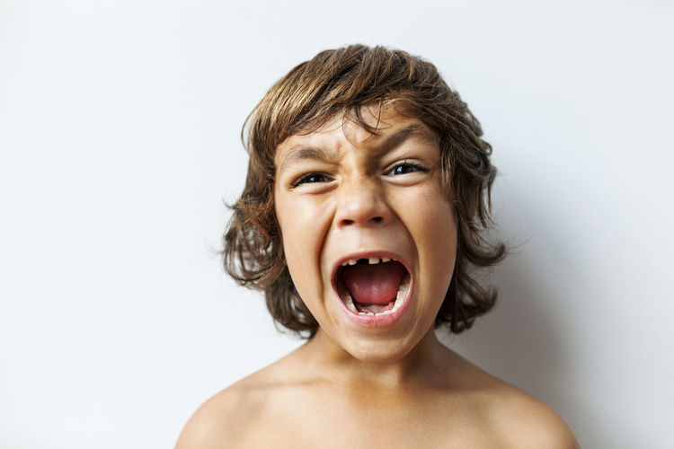 Portrait of screaming little boy with tooth gap in front of white background