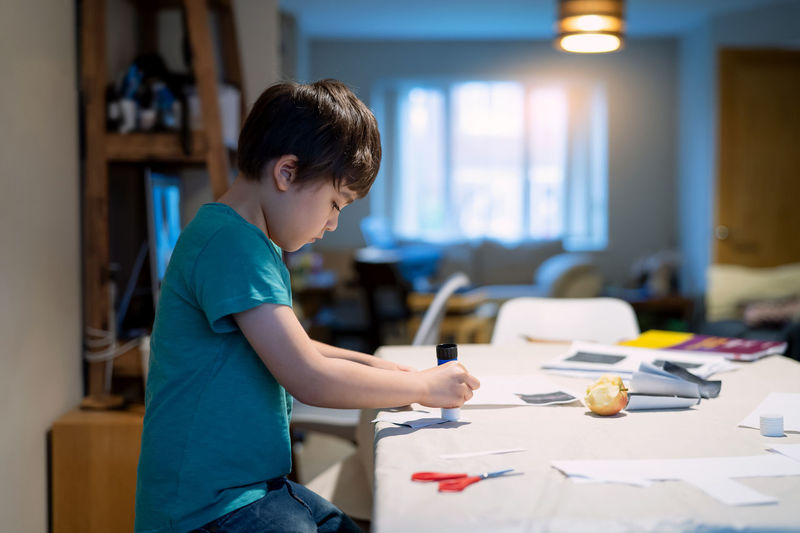 Side view of boy holding paper on table