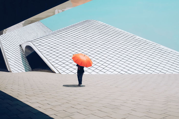 Low section of person with umbrella walking by modern building