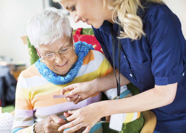 Caretaker filing senior woman's fingernails at nursing home