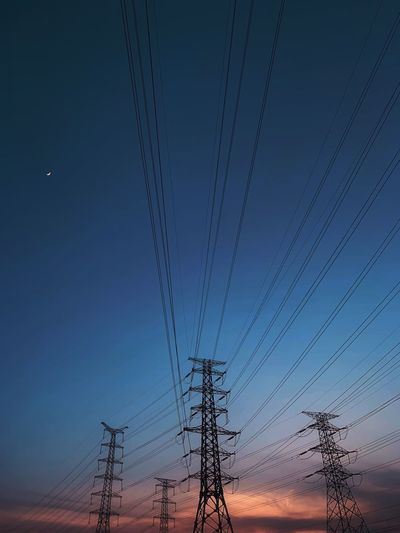 Low angle view of electricity pylon against sky at dusk