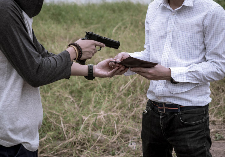 Midsection of criminal pointing gun at man while standing on field