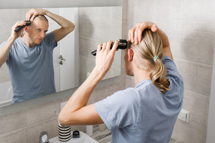 Personal hygiene, caucasian man cutting his own hair in the bathroom with wireless electric shaver