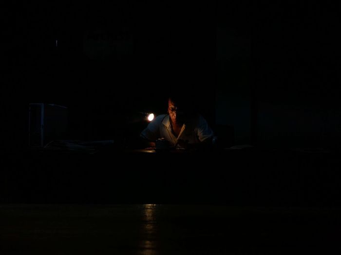 Man sitting in illuminated dark room