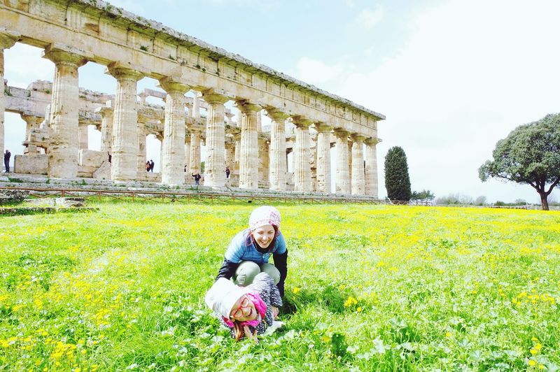 Mother and daughter playing on grassy field against old ruins