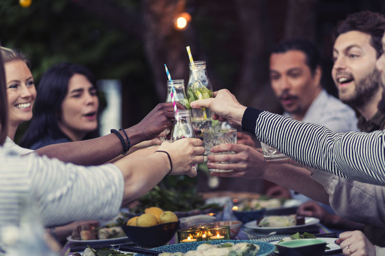 Happy friends toasting mojito glasses at table during dinner party in yard