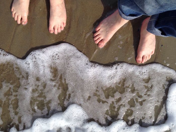Two pair of bare feet on sand await the wave