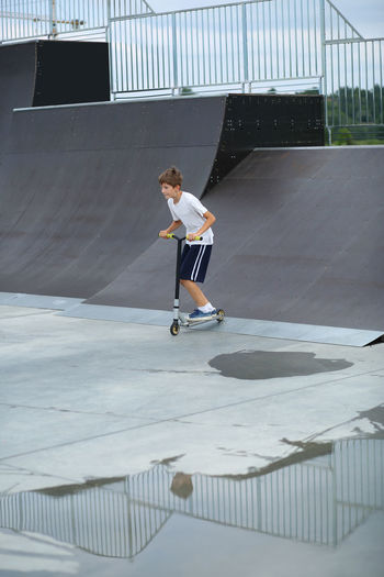 Active ten year old boy riding a scooter in the summer skate park