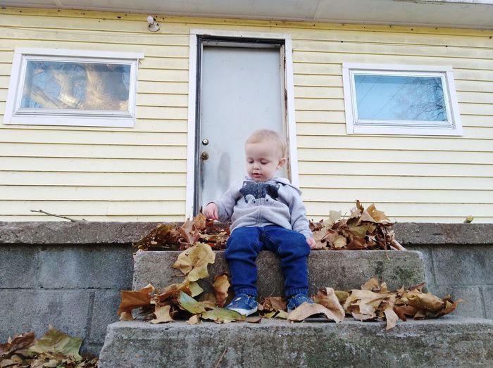 Full length of cute baby boy sitting on staircase against house